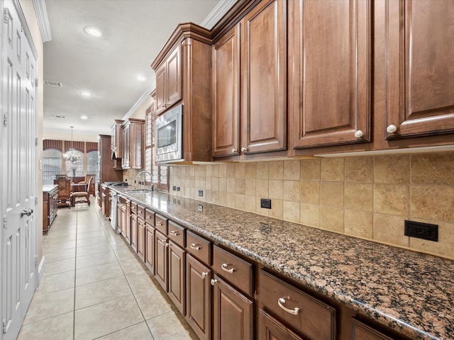 kitchen with stainless steel microwave, hanging light fixtures, dark stone countertops, ornamental molding, and sink