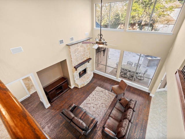 living room featuring a towering ceiling, ceiling fan, and a stone fireplace