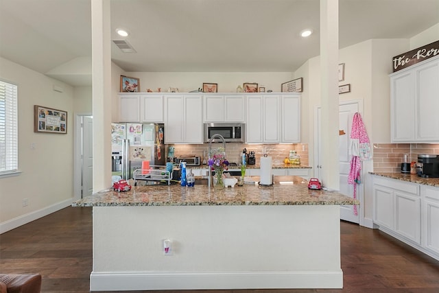 kitchen with light stone counters, a center island with sink, white cabinets, and stainless steel appliances