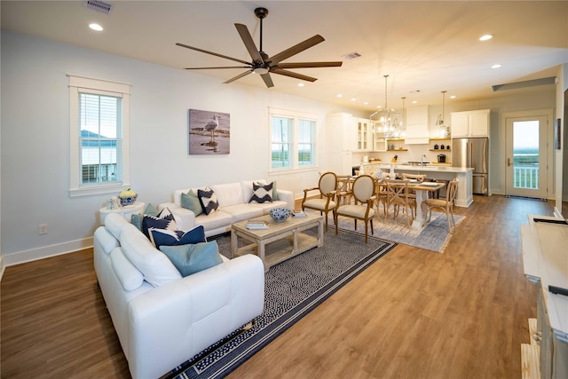 living room featuring ceiling fan with notable chandelier, plenty of natural light, and dark wood-type flooring