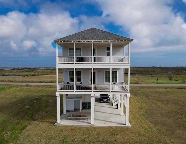 rear view of house with a lawn, a patio area, a balcony, and a rural view