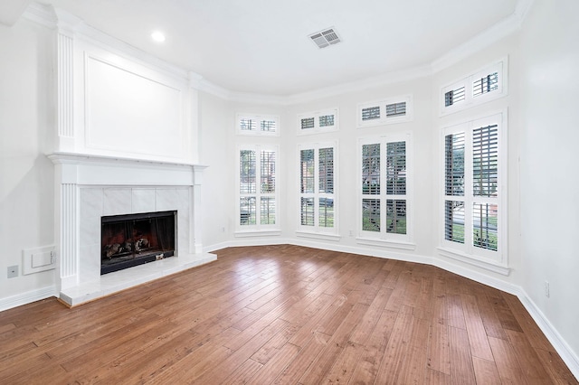 unfurnished living room featuring a tile fireplace, ornamental molding, hardwood / wood-style flooring, and a healthy amount of sunlight