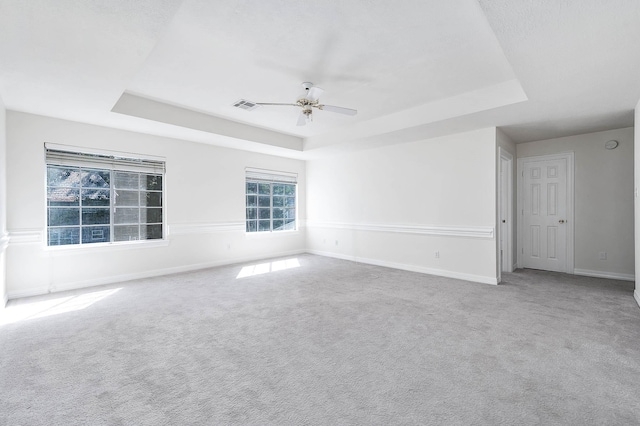 empty room featuring carpet, a tray ceiling, and ceiling fan