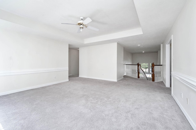 carpeted spare room with a tray ceiling and ceiling fan