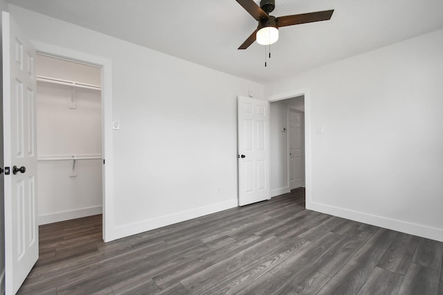 unfurnished bedroom featuring a closet, a spacious closet, ceiling fan, and dark wood-type flooring