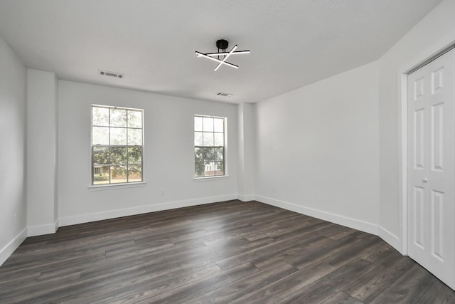 empty room featuring dark wood-type flooring and a notable chandelier