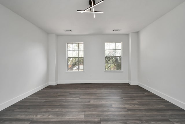 empty room featuring dark wood-type flooring and an inviting chandelier