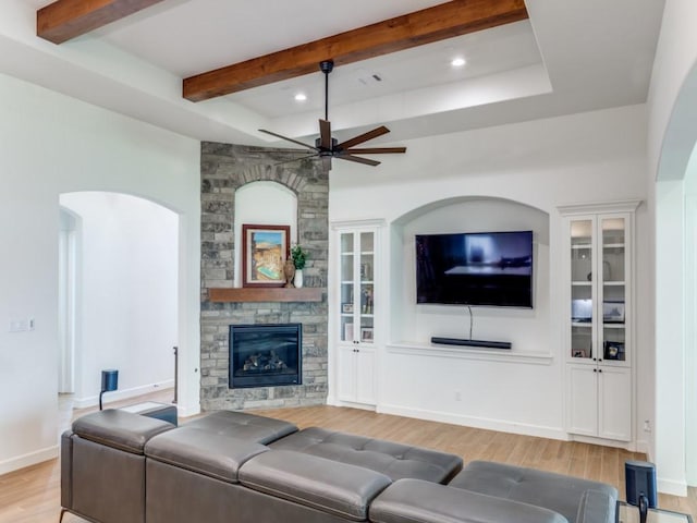 living room featuring ceiling fan, a fireplace, beamed ceiling, and light wood-type flooring