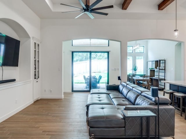 living room featuring beamed ceiling, ceiling fan with notable chandelier, and light hardwood / wood-style floors