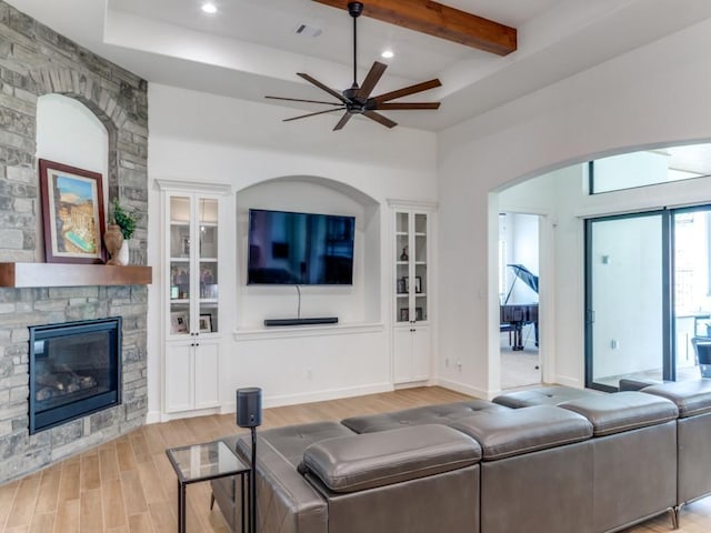 living room featuring a fireplace, beam ceiling, light hardwood / wood-style floors, and ceiling fan