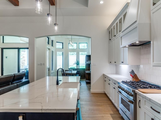 kitchen featuring sink, stainless steel stove, an island with sink, decorative light fixtures, and white cabinets