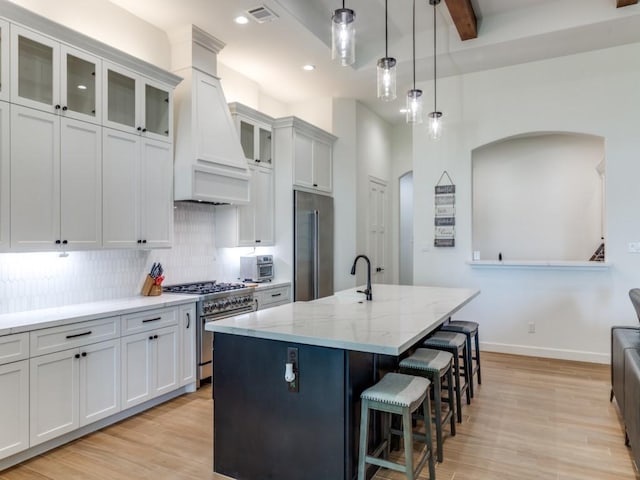 kitchen featuring white cabinetry, premium appliances, light stone counters, a center island with sink, and custom exhaust hood