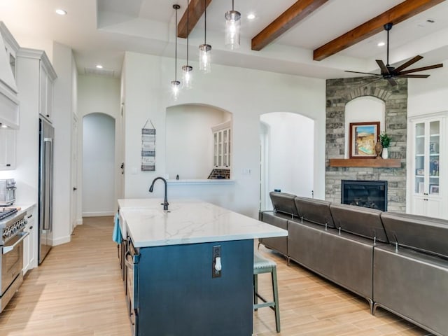 kitchen featuring stainless steel appliances, a stone fireplace, an island with sink, pendant lighting, and a breakfast bar