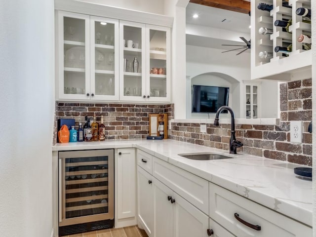 bar featuring light stone countertops, wine cooler, tasteful backsplash, sink, and white cabinetry