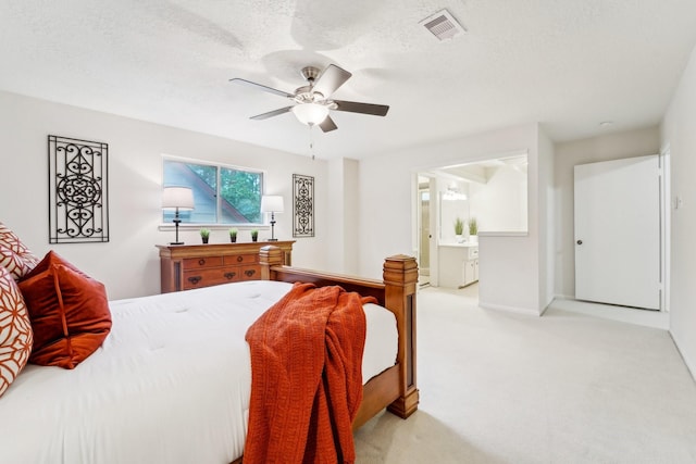 bedroom featuring ceiling fan, light colored carpet, a textured ceiling, and ensuite bath