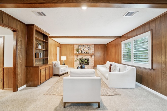 carpeted living room with beam ceiling, built in shelves, wood walls, a textured ceiling, and a fireplace