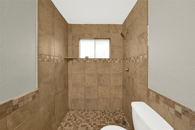 bathroom with tiled shower, toilet, and tile walls