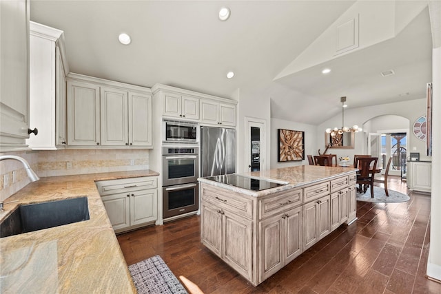 kitchen with lofted ceiling, sink, decorative backsplash, appliances with stainless steel finishes, and a kitchen island