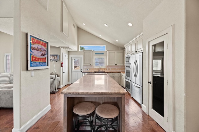 kitchen featuring a kitchen breakfast bar, dark hardwood / wood-style flooring, stainless steel appliances, vaulted ceiling, and a center island