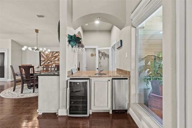 bar with pendant lighting, sink, wine cooler, light stone countertops, and a chandelier