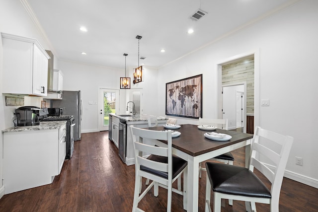 kitchen featuring a kitchen island with sink, sink, appliances with stainless steel finishes, decorative light fixtures, and white cabinetry