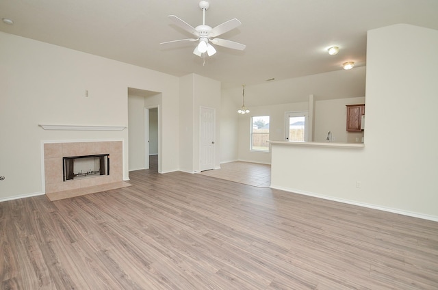 unfurnished living room featuring ceiling fan with notable chandelier, light hardwood / wood-style floors, lofted ceiling, and a tiled fireplace