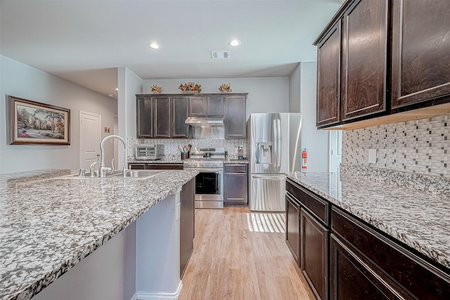 kitchen featuring tasteful backsplash, dark brown cabinetry, light stone countertops, and stainless steel appliances