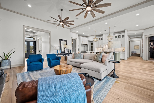 living room featuring sink, french doors, ornamental molding, light wood-type flooring, and ceiling fan with notable chandelier