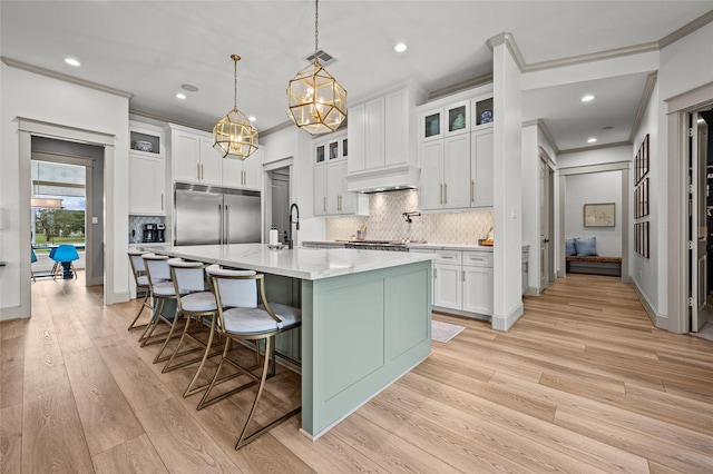 kitchen featuring pendant lighting, an island with sink, a breakfast bar, white cabinets, and stainless steel built in refrigerator