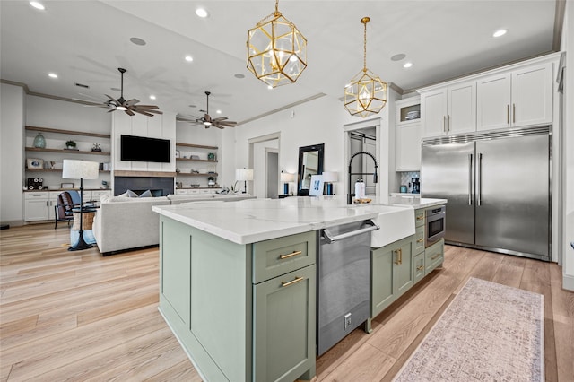 kitchen with built in appliances, decorative light fixtures, a kitchen island with sink, white cabinetry, and sink