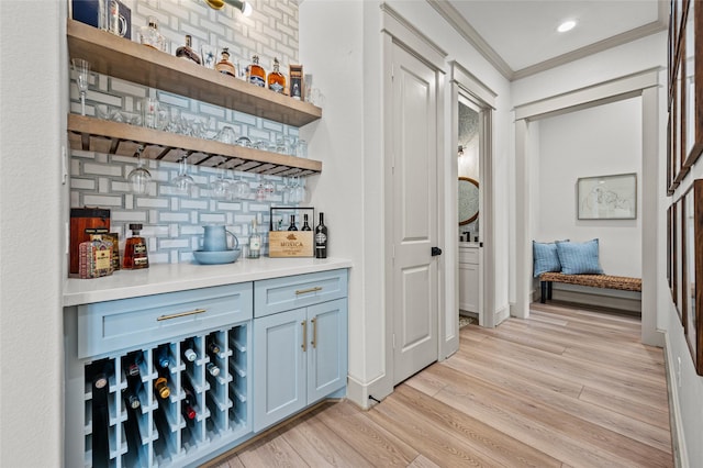 bar featuring ornamental molding, tasteful backsplash, and light hardwood / wood-style flooring