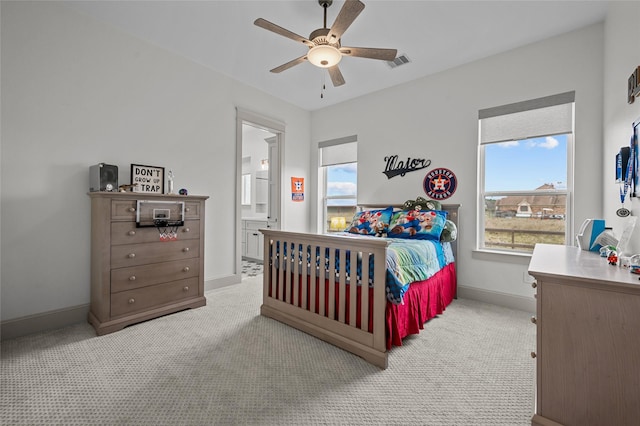 bedroom featuring ceiling fan, multiple windows, connected bathroom, and light carpet