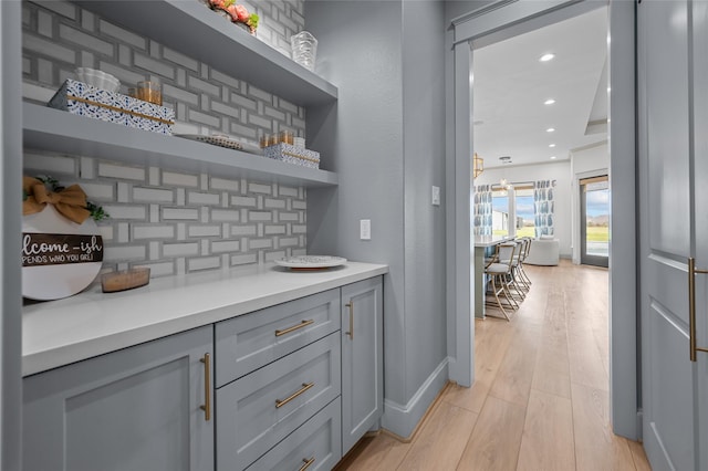 bar with light hardwood / wood-style floors, gray cabinetry, and backsplash