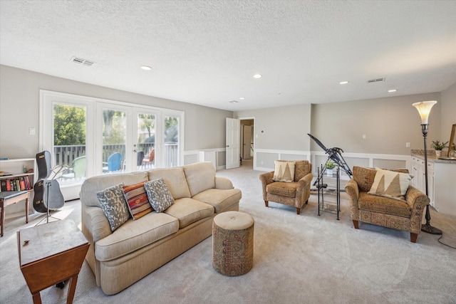 living room with french doors, a textured ceiling, and light colored carpet