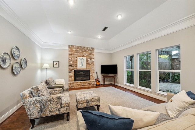 living room featuring a raised ceiling, wood-type flooring, and a brick fireplace