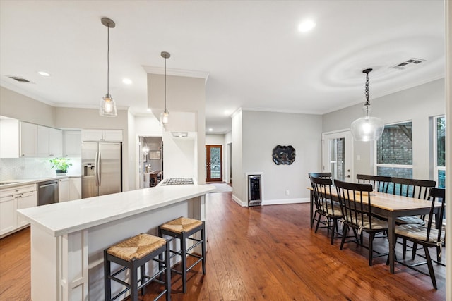 kitchen with a kitchen breakfast bar, backsplash, stainless steel appliances, pendant lighting, and white cabinets