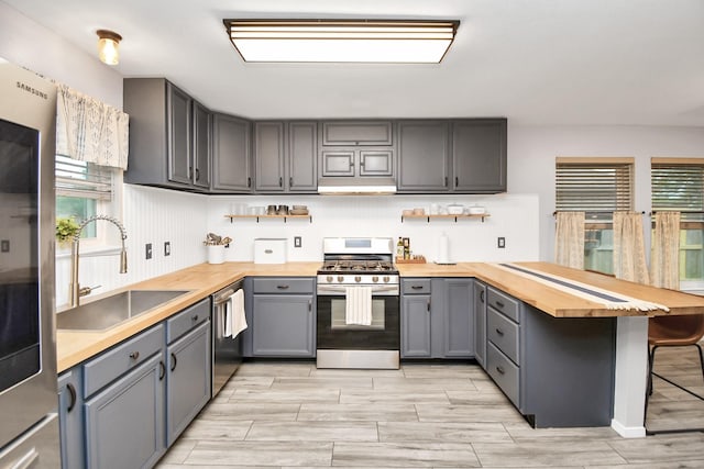 kitchen featuring appliances with stainless steel finishes, butcher block countertops, a kitchen breakfast bar, and sink