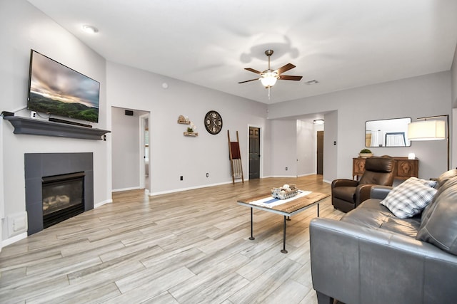 living room with ceiling fan, light wood-type flooring, and a tile fireplace