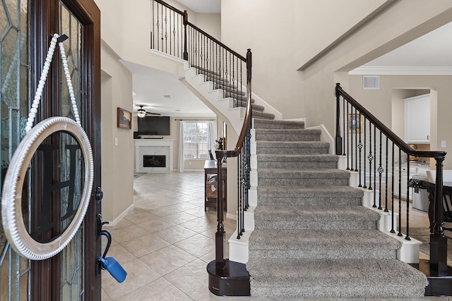 stairs with a premium fireplace, crown molding, and tile patterned flooring