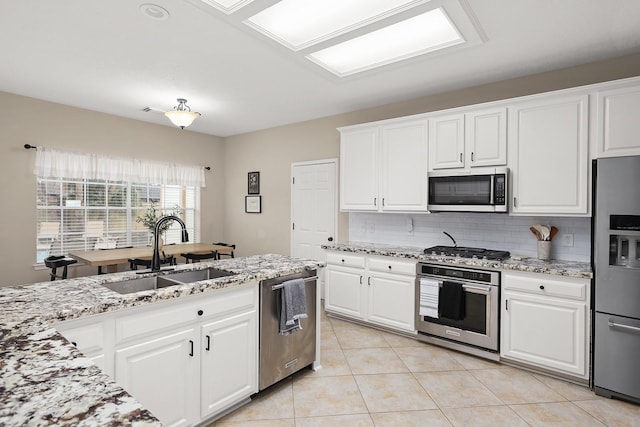 kitchen with light stone countertops, stainless steel appliances, sink, white cabinets, and light tile patterned flooring