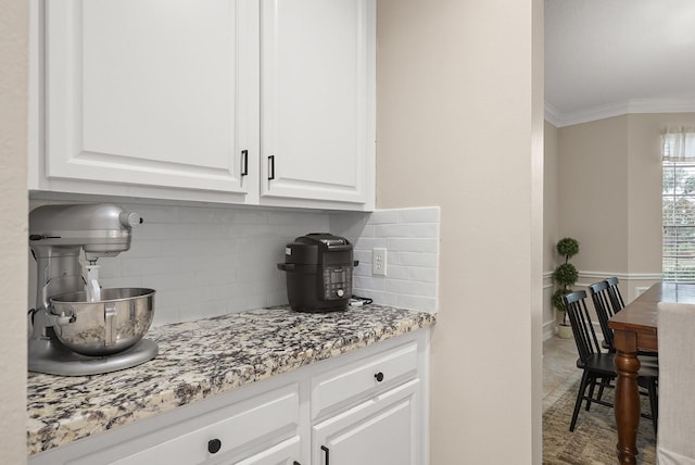 bar featuring decorative backsplash, light stone counters, white cabinetry, and ornamental molding