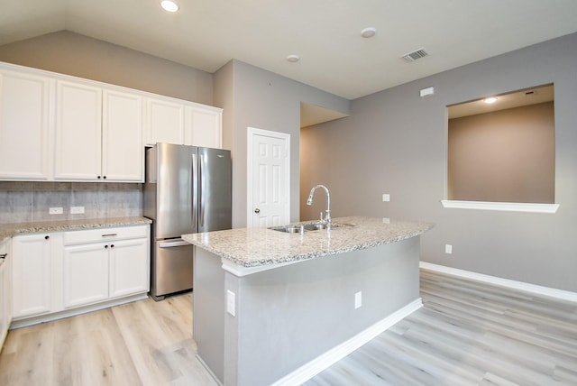 kitchen with white cabinets, stainless steel refrigerator, a kitchen island with sink, and sink