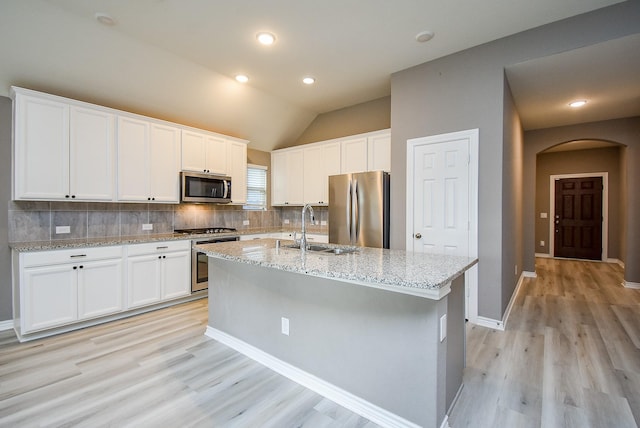 kitchen with appliances with stainless steel finishes, vaulted ceiling, a kitchen island with sink, sink, and white cabinetry