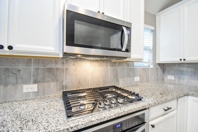 kitchen with white cabinets, light stone counters, backsplash, and appliances with stainless steel finishes