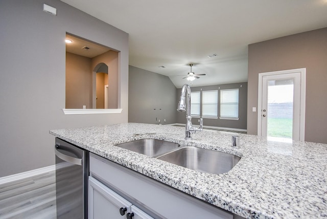 kitchen featuring light stone counters, stainless steel dishwasher, ceiling fan, sink, and light hardwood / wood-style flooring