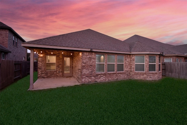 back house at dusk featuring a patio area and a lawn