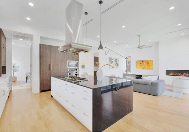 kitchen featuring stainless steel appliances, island range hood, pendant lighting, a center island, and white cabinetry