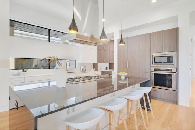 kitchen with island exhaust hood, dark stone counters, a breakfast bar, stainless steel appliances, and decorative light fixtures