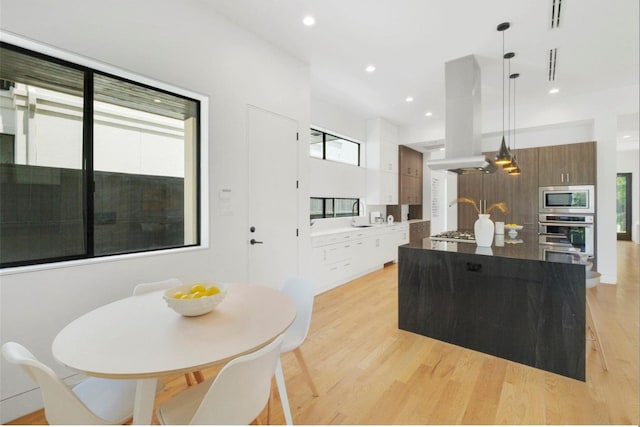 kitchen featuring island exhaust hood, appliances with stainless steel finishes, light wood-type flooring, pendant lighting, and a kitchen island