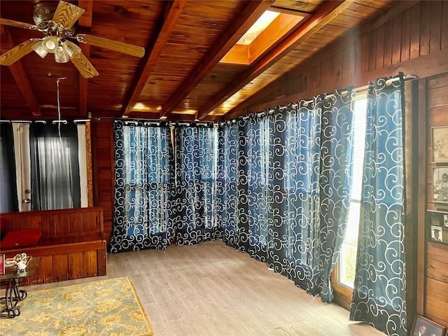 interior space with ceiling fan, a wealth of natural light, wooden walls, and lofted ceiling with beams